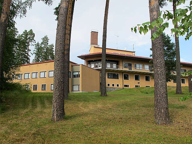 Yellow facade of the school viewed from between trees.