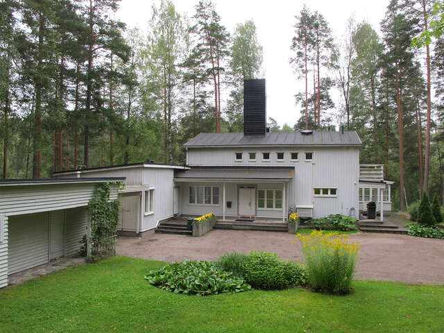 Light blue house in the forest with a lawn and flowers.