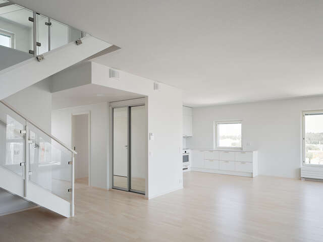 View of an apartment inside a hybrid football stadium, with a parquet floor, staircase, closet, and large white walls.