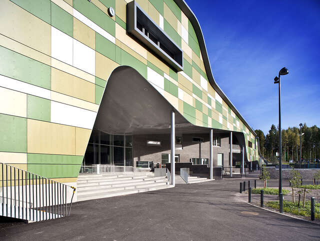 Different-sized cement composite panels in white and shades of green are used to create a vivid and playful patchwork. The facades are punctuated by protruding aluminium-framed windows.