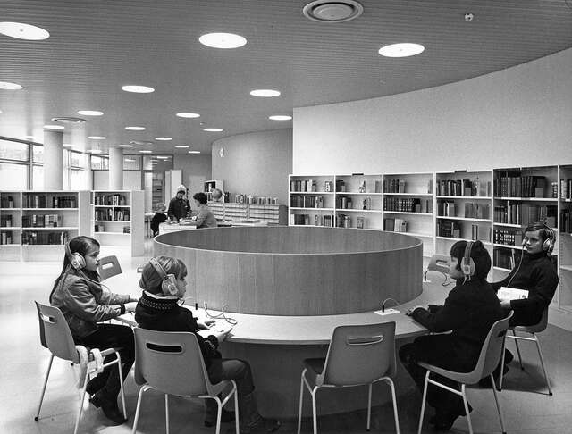 Children listening to music with headphones around a round table in a black and white picture.