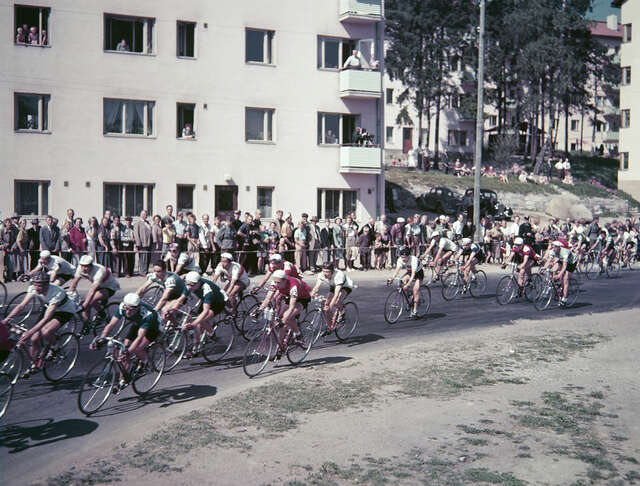 Road race and crowd standing in front of a lamel house.