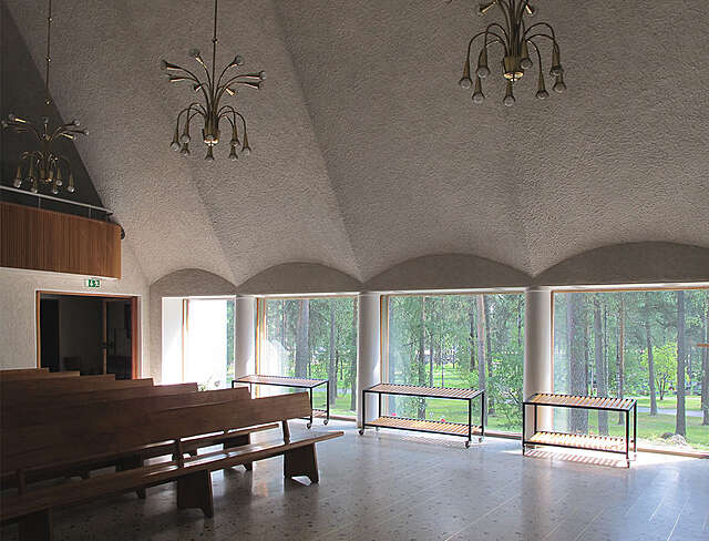 Chapel with a white plastered ceiling and large windows covering the whole wall, benches are positioned on the right.