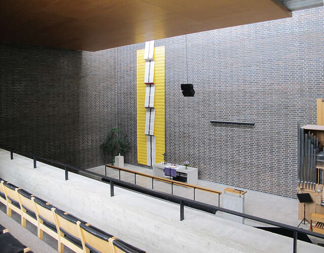 Inside a cube-like space with pews, altar and skylight