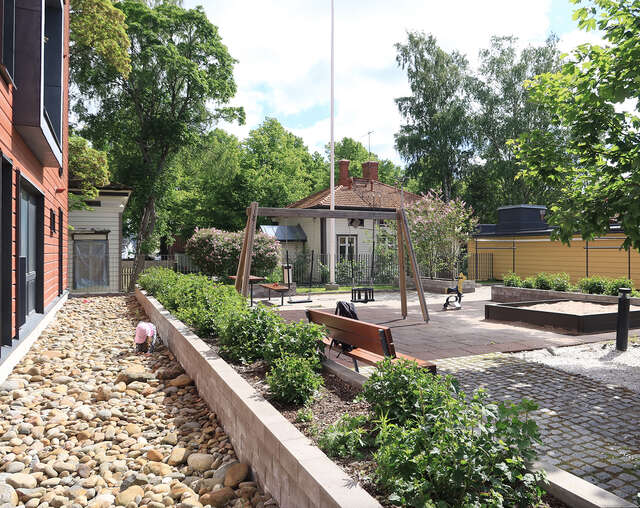 Playground in front of a red block of flats. Old wooden house in the background.