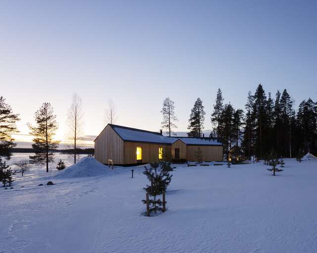 The house in a soft evening light, surrounded by snow, a frozen lake on the background.