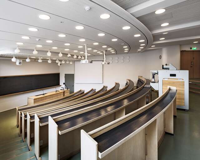 Lecture hell with curved seating rows, white ceiling and walls and a backboard at the back.