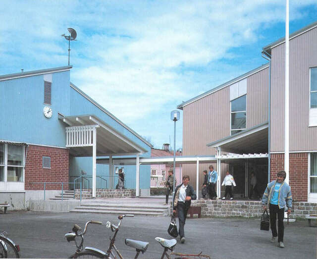 Entrance yard of the schoo, bicycles and pupils in the foreground.