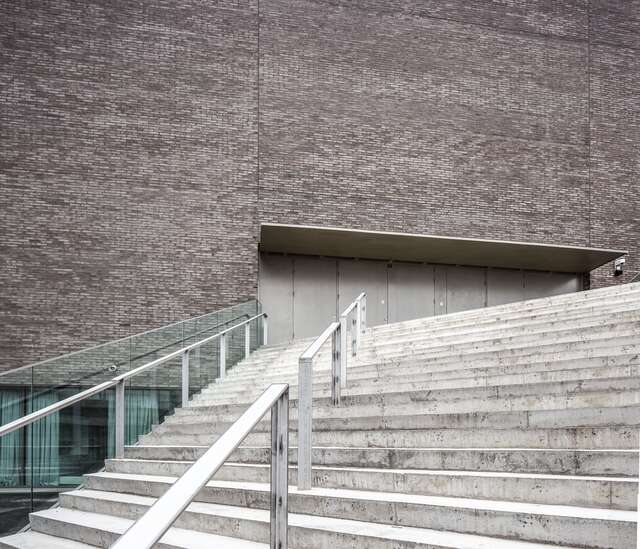 Concrete stairs with metal and glass railings, a grey-brick building in the background.