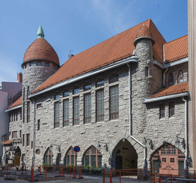 Stone facade of an old building with arch details and a tower.