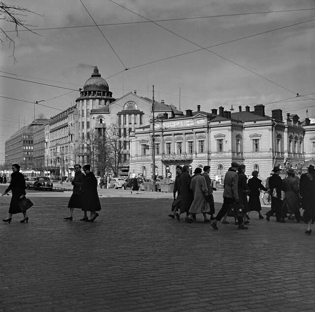Black and white picture of pedestrians walking on the street and the New Student House in the background.