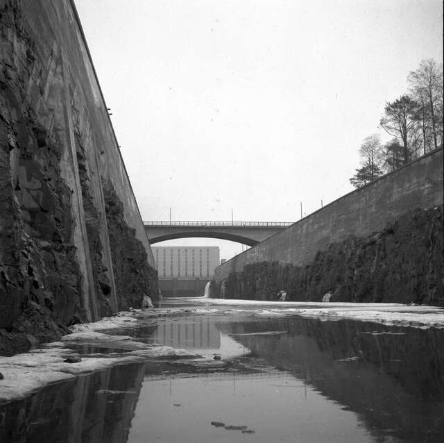 BW photo from nearly water level in a canal, further down a bridge and a big building at the end of the canal