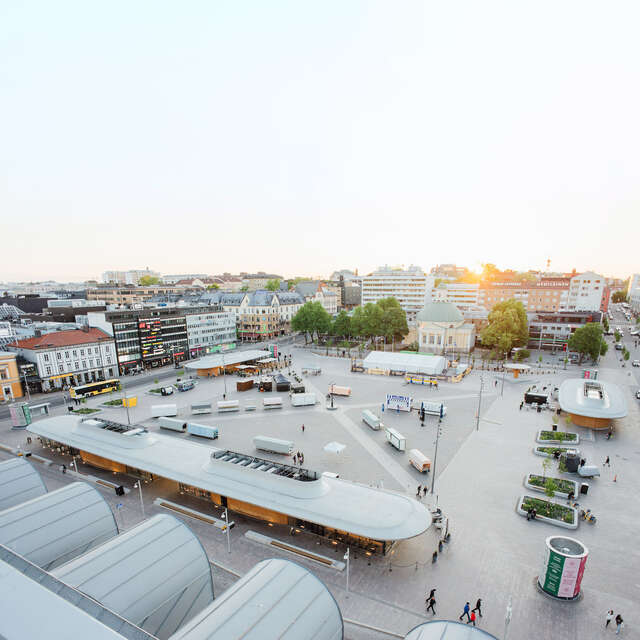 A large open market area in the middle of a city as seen from a nearby rooftop during sunset.