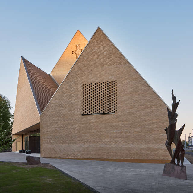 Wooden sharply shaped building standing in an asphalt yard in a blue light and a clear sky on the background.