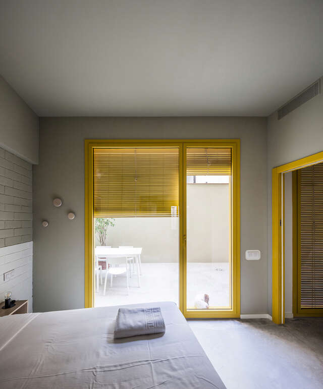 A bedroom of an apartment. There is a window with yellow shades and window frames.