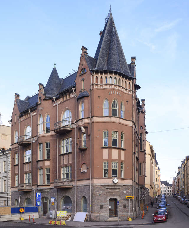 Brown city house at the corner of a street with a tower at the top.