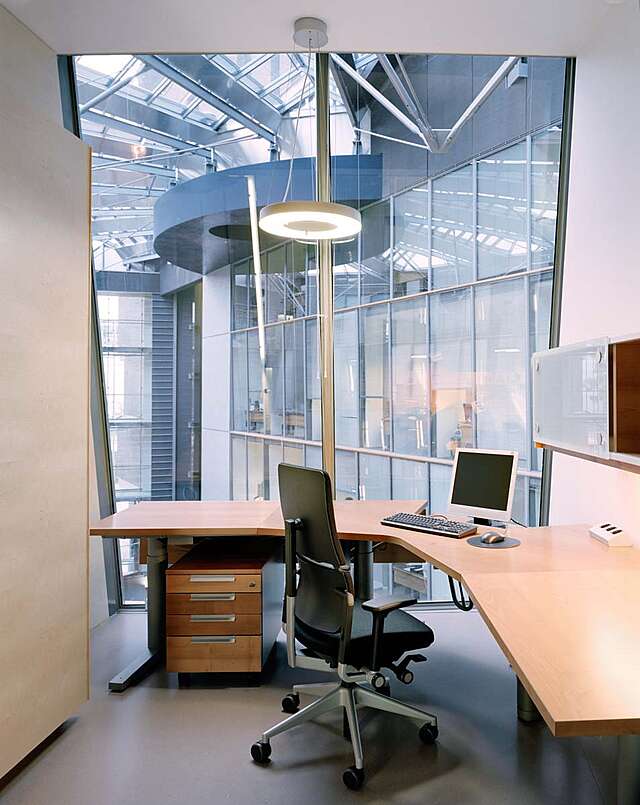 Room with office furniture and a large window with a view to an atrium
