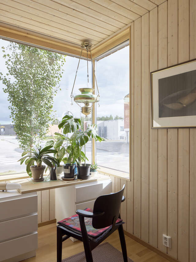 A room with a corner window looking outside. A chair and table with plants on in is in front of the window.
