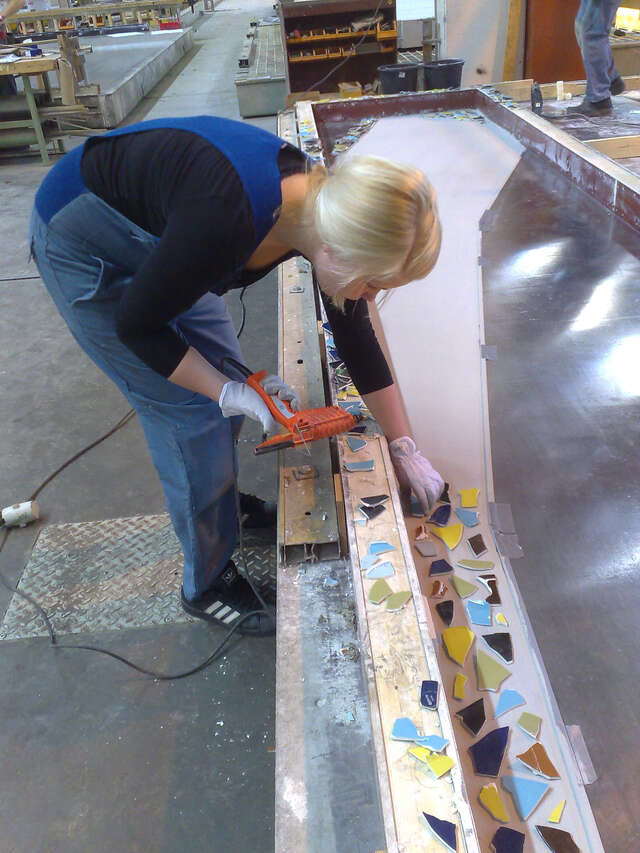 Young woman glueing mosaic pieces on a light surface.