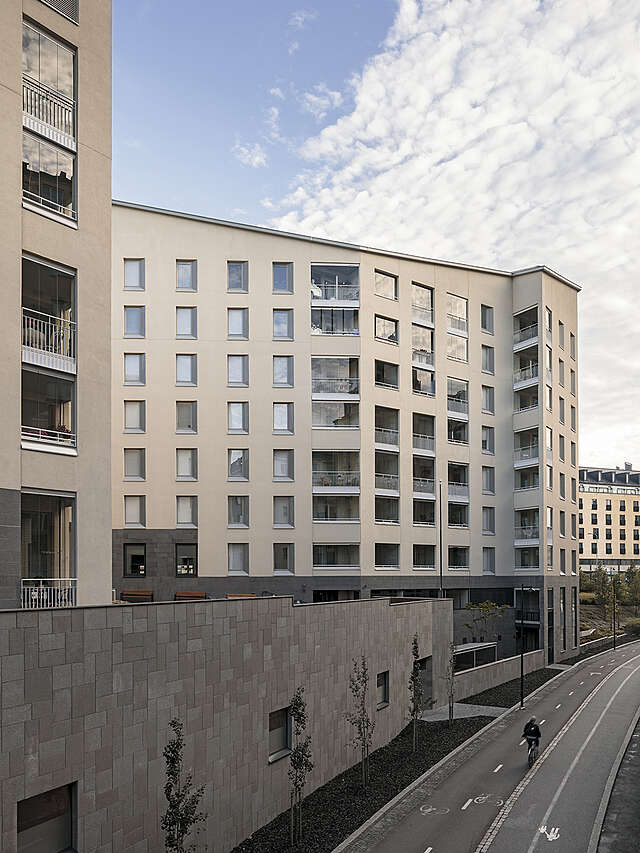 Beige plastered modern apartment building with a stone fence separating it from the street.