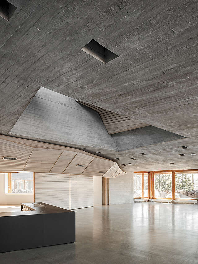 Entrance with a reception desk, a concrete ceiling and orange framed windows.