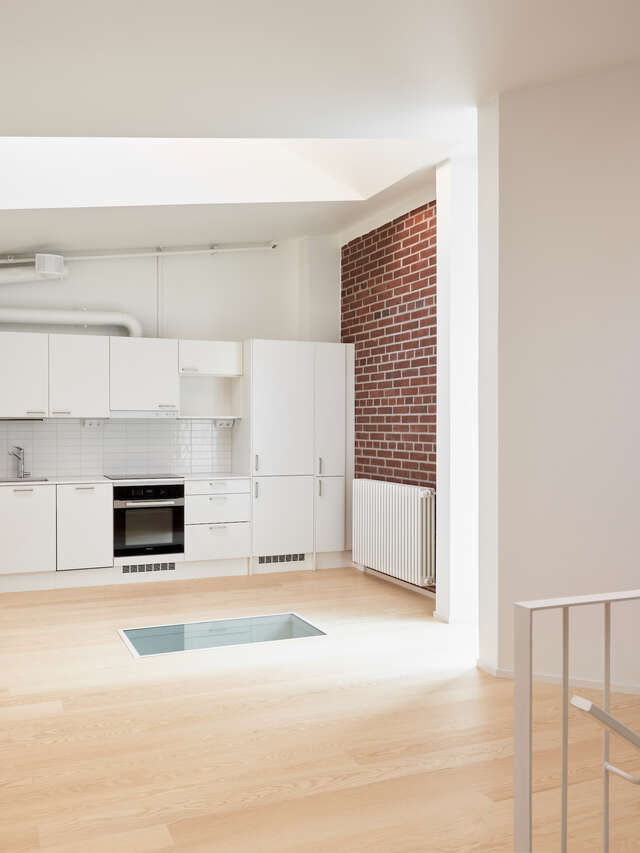 A white kitchen with a brick wall and wooden flooring.