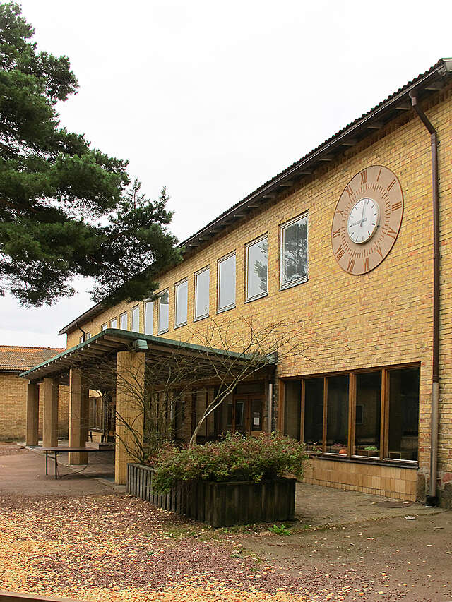 Yellow-Brick facade with a large clock, the yard is covered in fallen leaves.