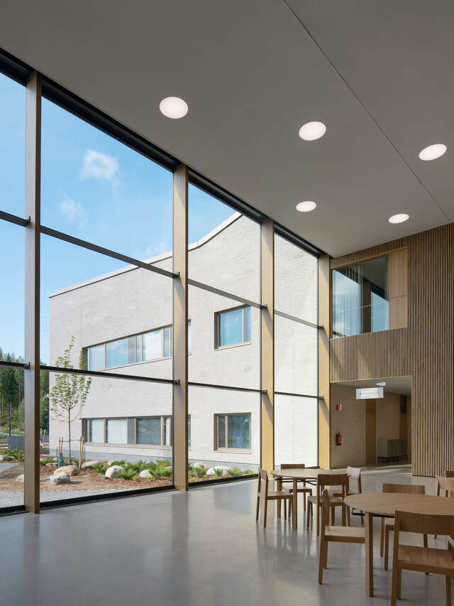 A large window panel wall showcasing a large stone structure. Groups of tables and chairs are inside the building.