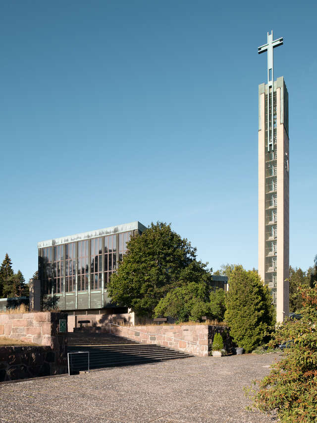 A square building next to a tower with a cross on it as seen from outside.