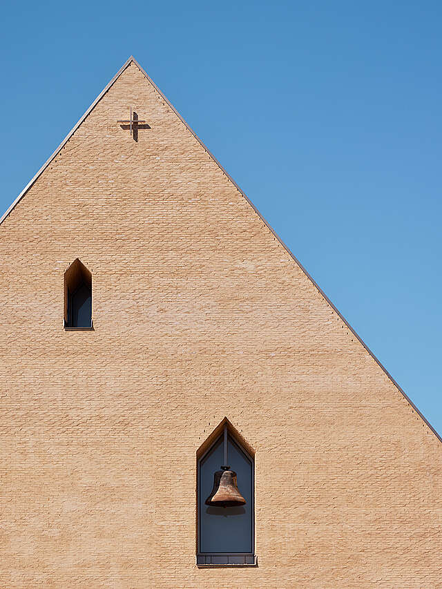 Detail of a yellow-brick gable with a niche for a bell and a small cross on top
