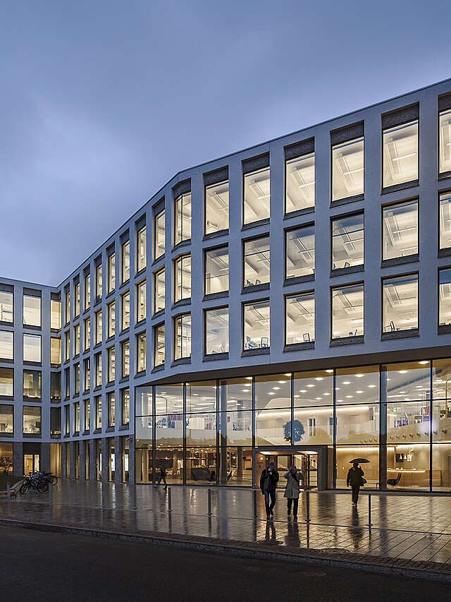 White plastered office building facade with large windows and a glass wall at the entrance.