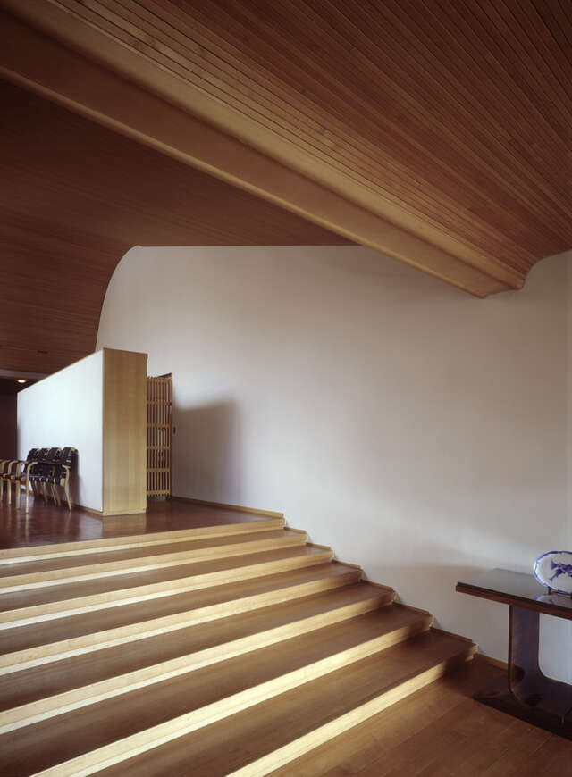 White wall in between of wooden rising stairs and curved ceiling