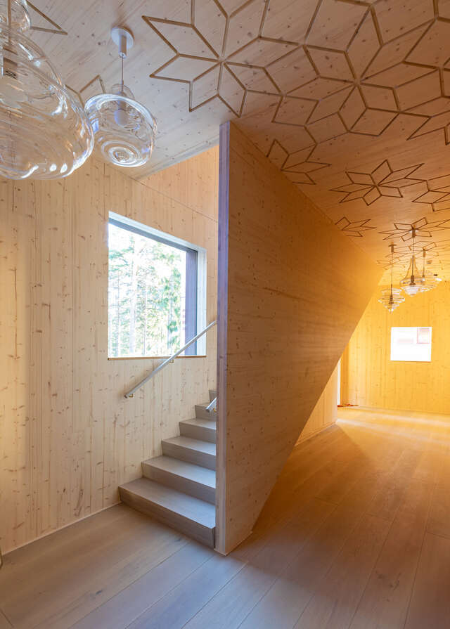 A staircase and lobby space built entirely of wood. Decorative carvings on the ceiling, with hanging glass lamps.