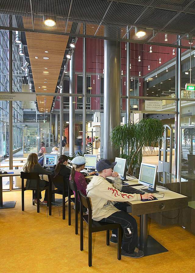 Children sitting in front of library computers, the entrance hall is visible through the glass wall.
