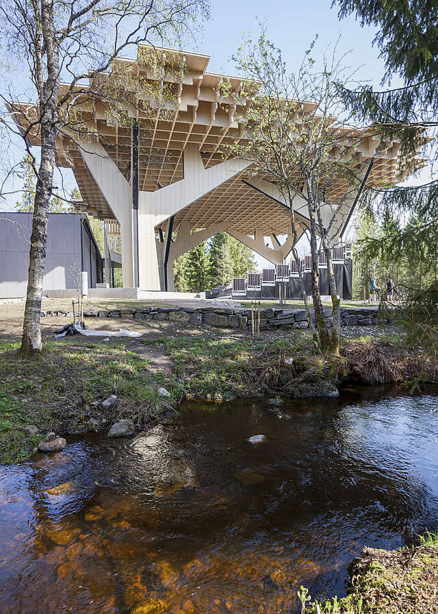A view over water towards a wooden, mushroom-like canopy