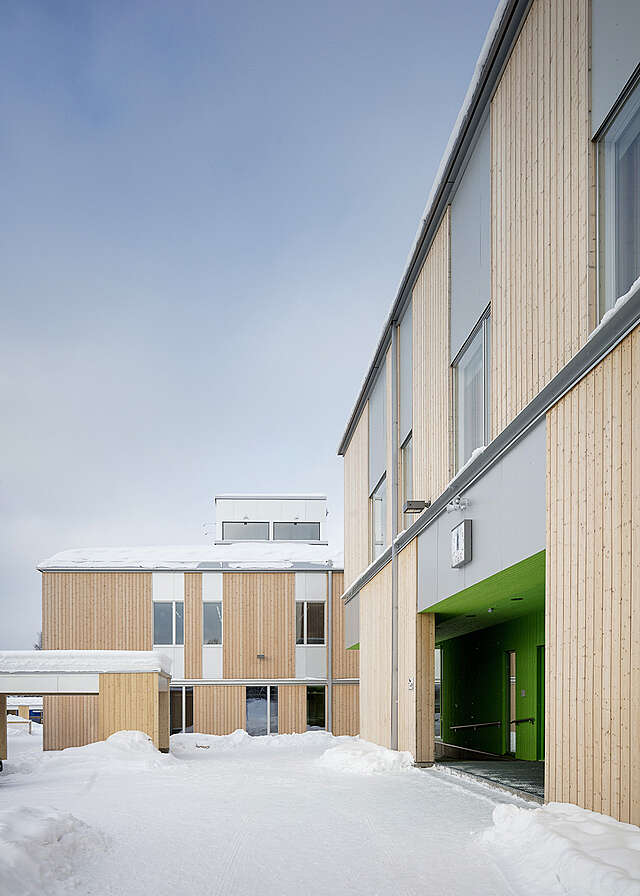 Snowy school facade with wood and metal paneling.