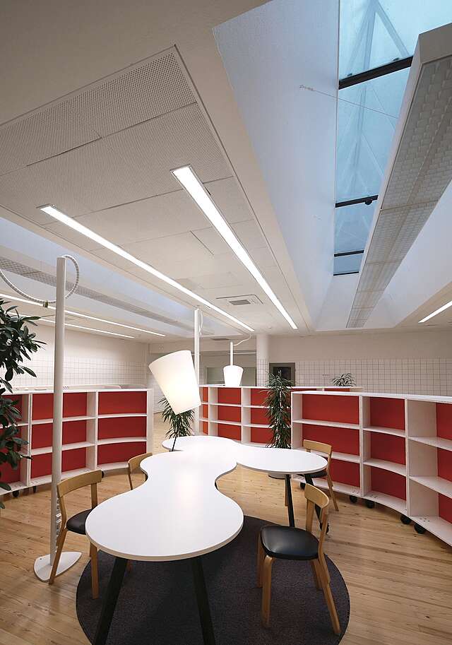 White curved table at the middle of the room, low bookshelves with red backgrounds.