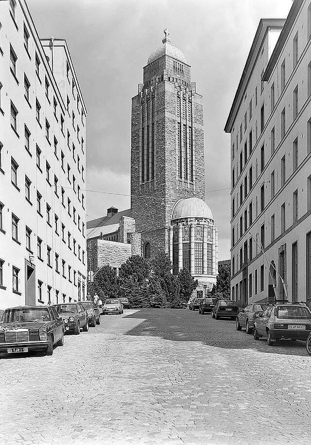 Residential street with parked cars, church tower centered