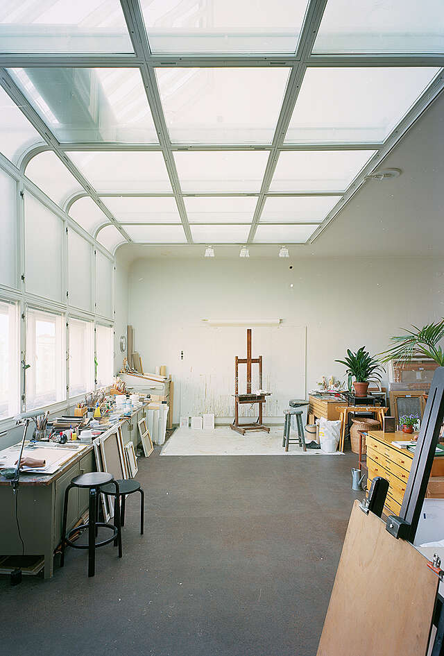 Art studio with messy work spaces and large windows extending to the ceiling.