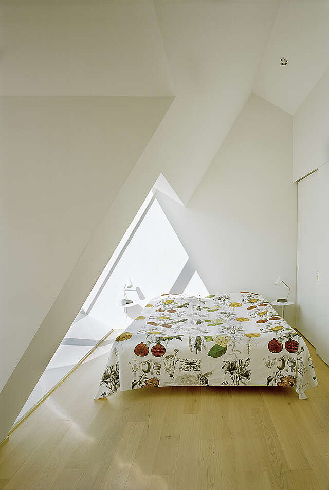 White bedroom with a slanted wall with a window on the left and a double bed with side tables on each side in the middle.