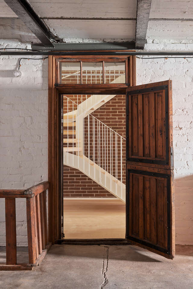 An old wooden door opening to a view of a hallway with a staircase.