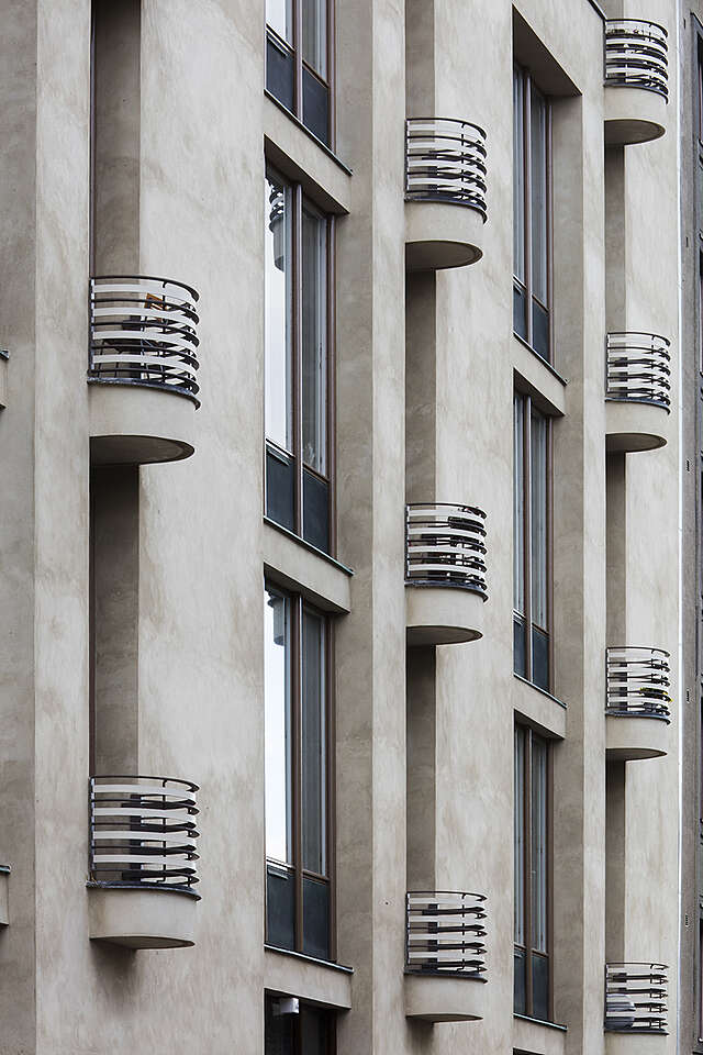Gray plastered facade with semi circle metal wire balconies.