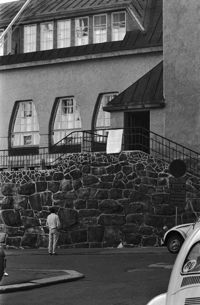 Man stands in front of the stone wall of the school.