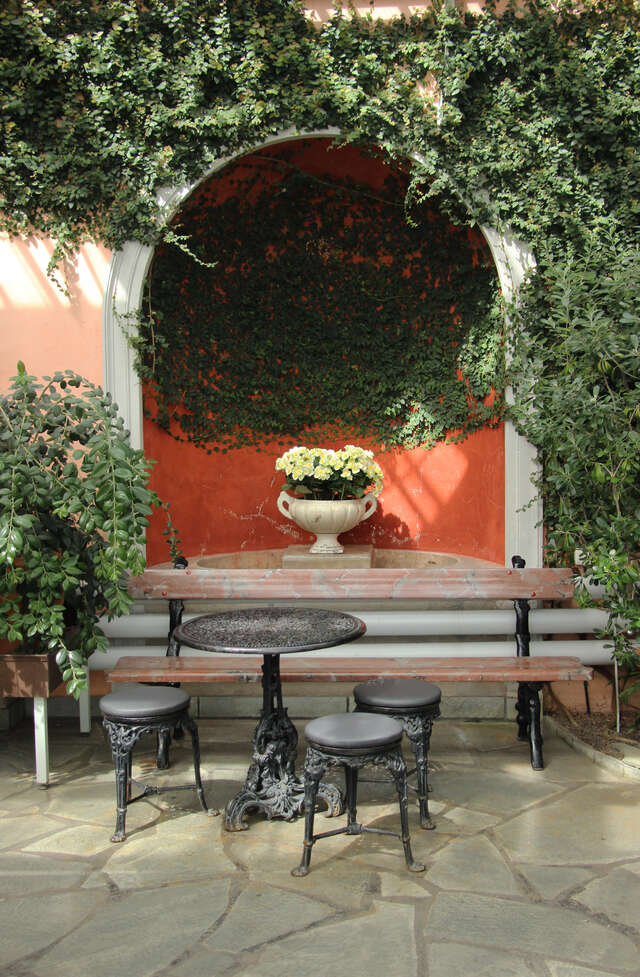Arch shaped indentation in the wall with flower pot inside of it. In the front there is a bench and a table.